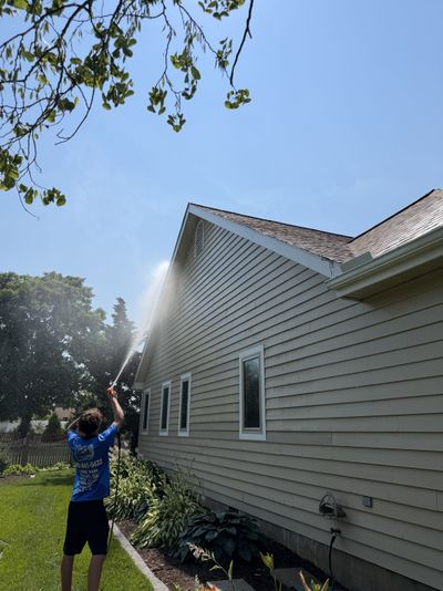 A technician rinsing the soffit and roofline of a home during a soft wash