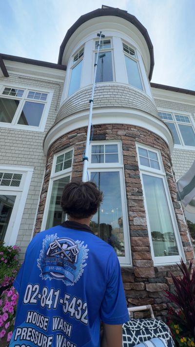 A technician using a water-fed pole to wash tall turret windows on a large coastal home