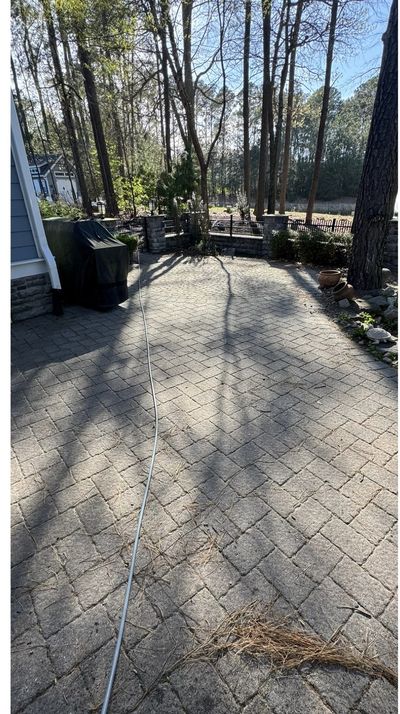 A paver patio under trees with pine needles and grime before cleaning
